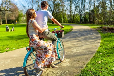 Romantic couple enjoying a leisurely bike ride through a sunny park, embracing the simple joys of