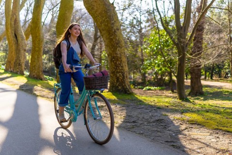Young woman riding a vintage bicycle through a sunlit park, enjoying the fresh air and vibrant