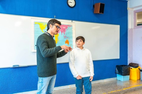 Geography teacher explaining lesson to elementary school student using a world map in a classroom
