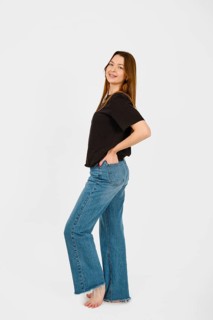 Barefoot woman stands with a playful posture, smiling at the camera while wearing a black top and