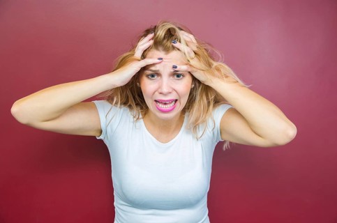 Concept of worry, woman with both hands on head on red background
