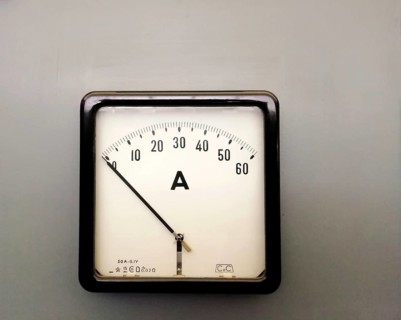 A large square industrial ammeter with an analogue dial with numbers with standard electrical