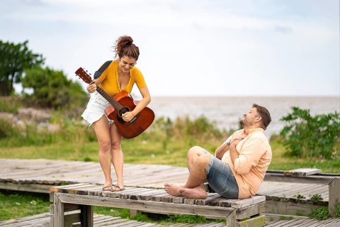 Man touches his chest in emotion as he listens to his girlfriend play guitar
