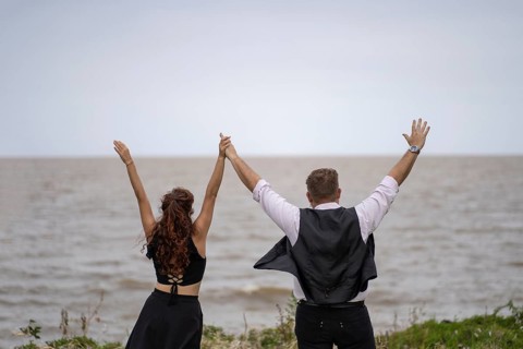 View of a couple from behind celebrating with their arms raised looking at the horizon in the sea