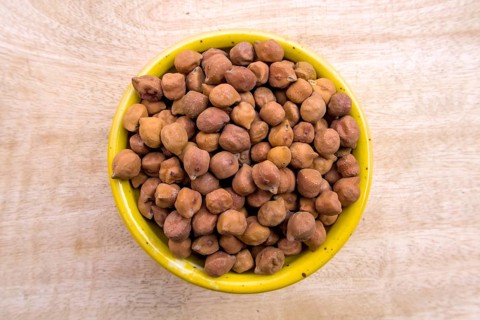 Flat Lay of Black Brown Chickpeas in a Yellow Bowl on Neutral Wooden Background, Top View