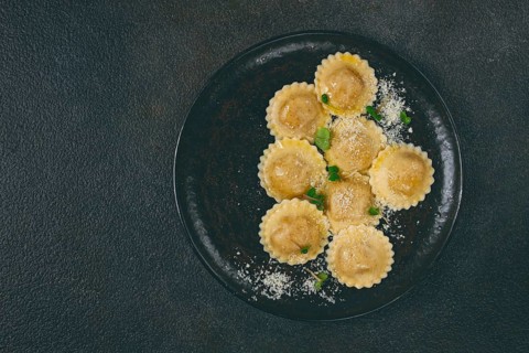 Fresh ravioli with cheese and microgreens, on a black plate, top view, no people