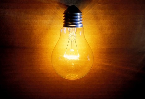 Closeup of an old burning light bulb, switched on, a carton as background is illuminated, lit with