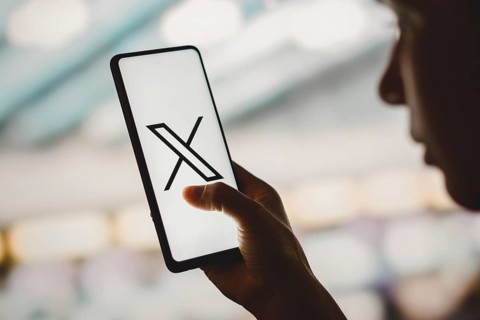 In this photo illustration, a silhouetted woman holds a smartphone with the Twitter (X) new logo