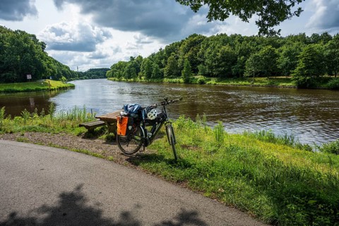A bicycle stands on a cycle path next to a peaceful river in nature, cycle tour along the Ems and