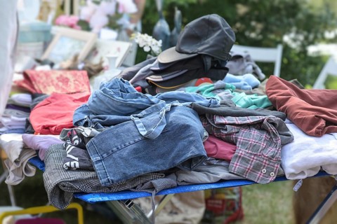 Used clothes and caps for sale at a flea market or garage market on a sunny weekend day, copy