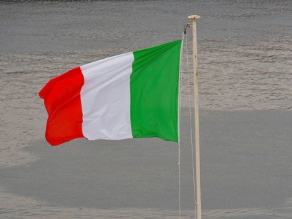 Italian flag waving in the wind in front of a body of water, naples, mediterranean sea, italy