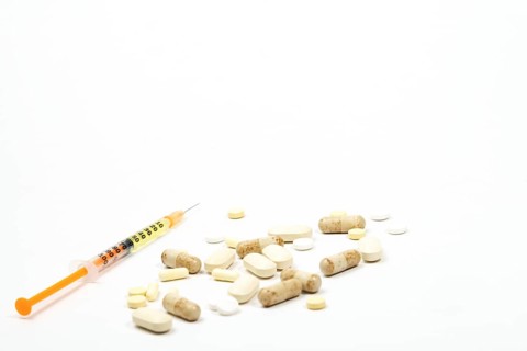 Syringe with vaccine next to a group of pills on white background and copy space