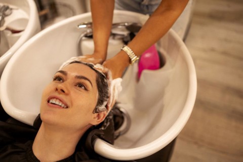 Cheerful young brunette womn enjoying head massage and washing hair while getting her haircare