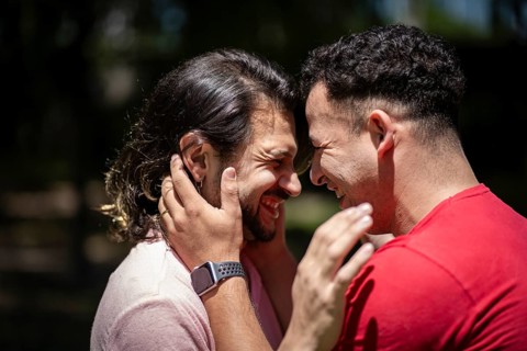 Couple of latin men hugging each other putting their heads together laughing in a park