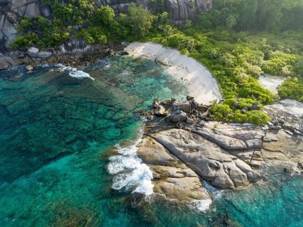 Coastline with waves, large rocks and tropical vegetation on turquoise water, aerial view,