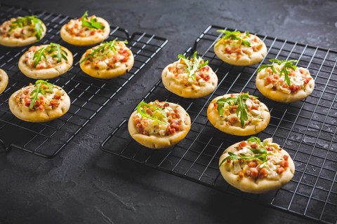 Small tarte flambee or mini pizza with onion, bacon and arugula on black background