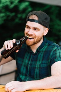 Man opening beer bottle cap with his teeth