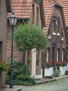 A quiet alley with brick houses, a alleyway lamp and a tree, flowers hanging from the windows,