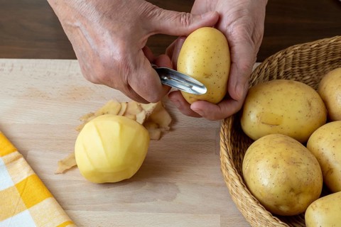 Hands peel potato, peelings on wooden cutting board