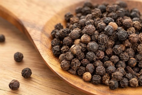 Black pepper (Piper nigrum) or pepercorn on wooden spoon. Cooking Spices.