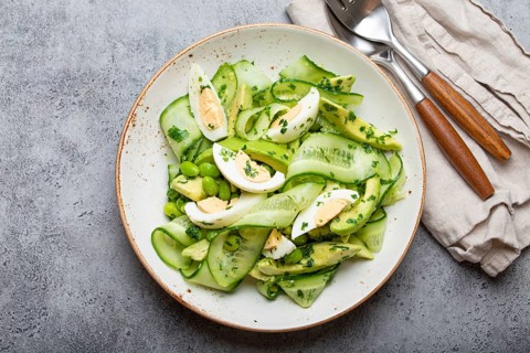 Healthy green avocado salad bowl with boiled eggs, sliced cucumbers, edamame beans, olive oil and