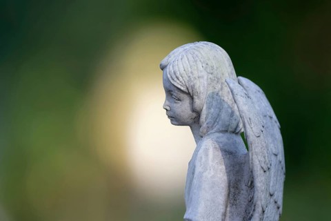 Sad looking little angel figure on a gravestone in front of atmospheric bokeh in the background