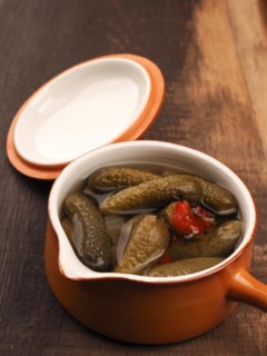 Organic gherkins in a rustic ceramic bowl on a wooden kitchen table, healthy food