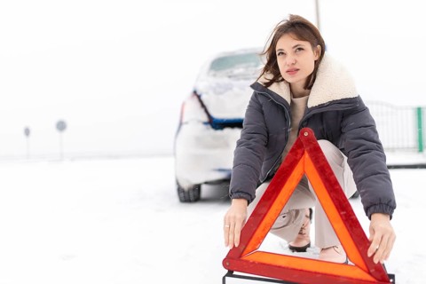 Woman puts up a warning triangle on a snowy road in winter, car breakdown in winter