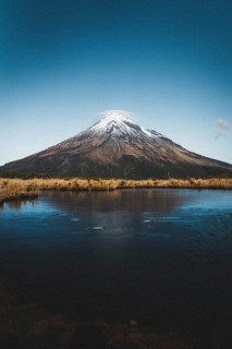A snow-capped mountain reflected in a still lake under a clear blue sky, Mount Taranaki, New