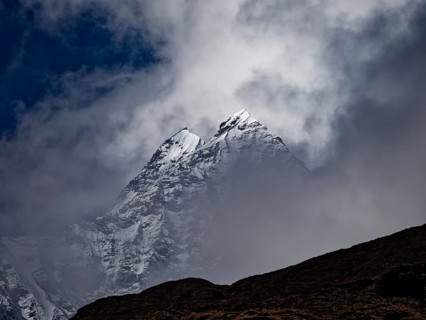 Two brightly lit snowy peaks peeking out of the clouds behind a dark ridge, Annapurna region,