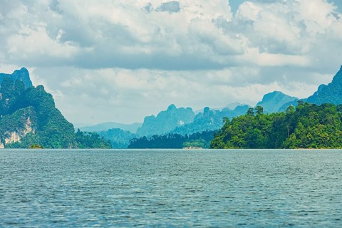 Distant mountains on a cloudy horizon overlook a vast lake, offering a calm natural scene, Cheow