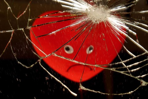 Red heart with a sad face reflected in a broken mirror with a black background