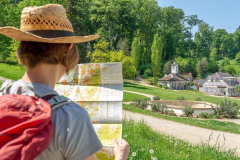 Woman with brown hair, gray t-shirt, jeans, red backpack and straw hat taking a break from her
