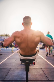 A man exercises outdoors in the sunlight, concentrating on strengthening his back muscles on a