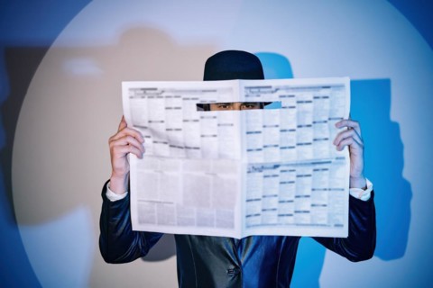 Man hiding watches through the newspaper in the spotlight on studio background. noir film style.