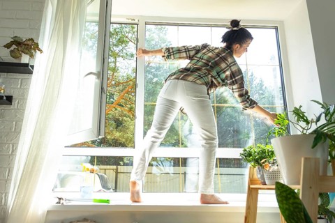 Woman manually washes the window of the house with a rag with spray cleaner and mop inside the