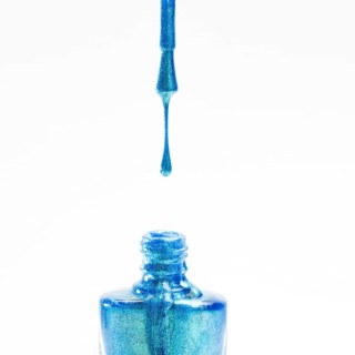 Glitter blue nail polish falling into bottle white background