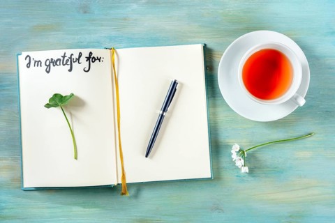 Open gratitude journal with a pen and a cup of tea, with the handwritten phrase I am grateful for