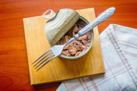 An open tuna box on a wooden board, with a fork and a towel