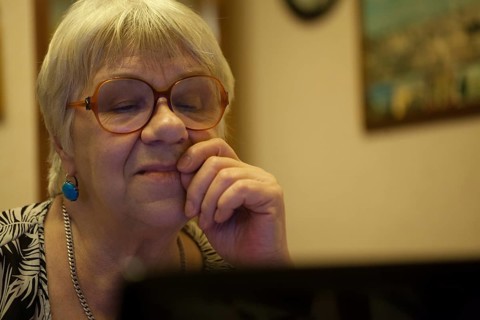 Thoughtful senior woman with blond hair wearing spectacles reading a computer screen with her hand