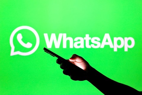 In this photo illustration the WhatsApp logo seen in the background of a silhouette hand holding a