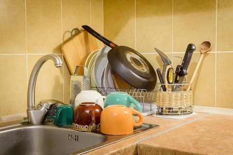 Dishes, cups, glasses, plates, forks, knives and spoons are drying close to the sink, after they