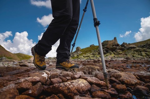 Hiking boots close-up on mountain rocks by the lake with trekking poles, view from below