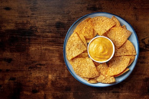 Nachos, Mexican tortilla chips, shot from above on a wooden background with a cheese dip
