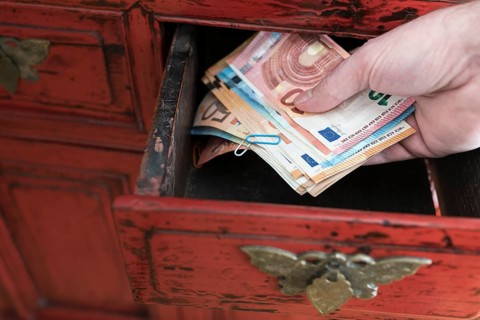 hand taking stack of paper money from drawer of antique cabinet
