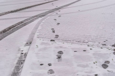 Fresh snow covers a cobblestone street with footprints and tire tracks crossing, creating a winter