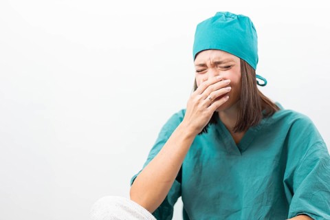 Emotional nurse in teal uniform crying on a white background