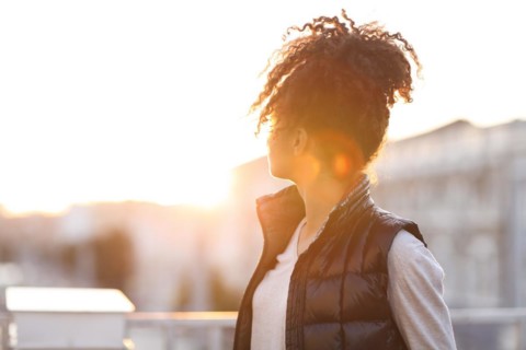Rear view of young woman standing at rooftop in morning sunlight, african american female standing