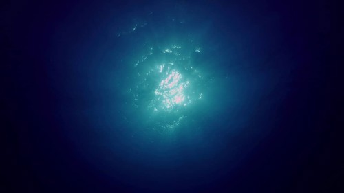 View of sun light from blue abyss, slow motion. Light filters down through blue water. Underwater