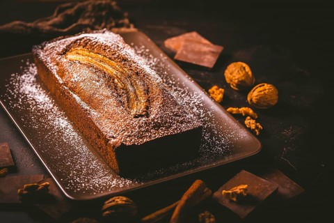 Homemade vegan banana bread or cake with nuts, chocolate and cinnamon on brown background